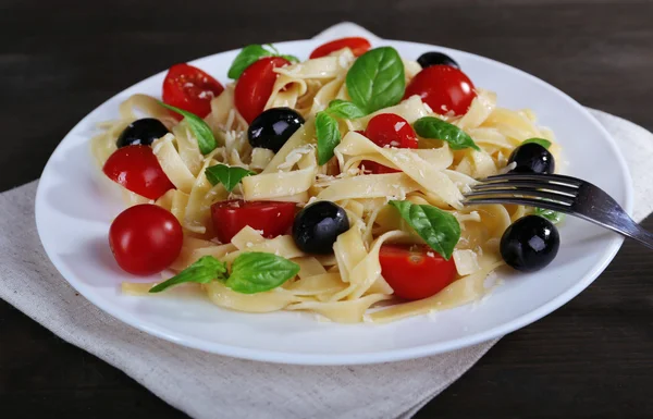 Spaghetti mit Tomaten, Oliven und Basilikumblättern auf Teller auf Holzgrund — Stockfoto