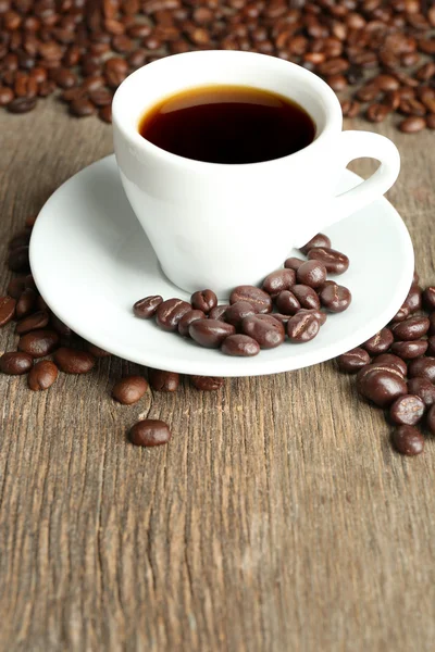 Xícara de café e grãos de café com esmalte de chocolate em fundo de madeira — Fotografia de Stock