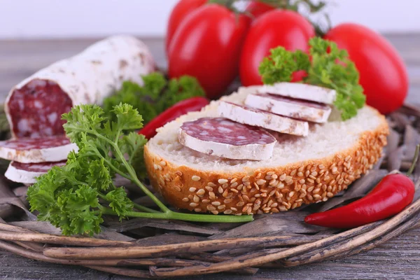 Французская салями с помидорами, хлебом и петрушкой на плетеном коврике на деревянном фоне — стоковое фото