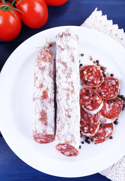Salame francese su piatto su tovagliolo con pomodori su fondo di legno blu scuro — Foto Stock