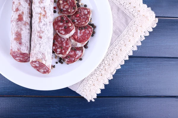 Französische Salami auf Teller auf Serviette auf dunkelblauem Holzhintergrund — Stockfoto