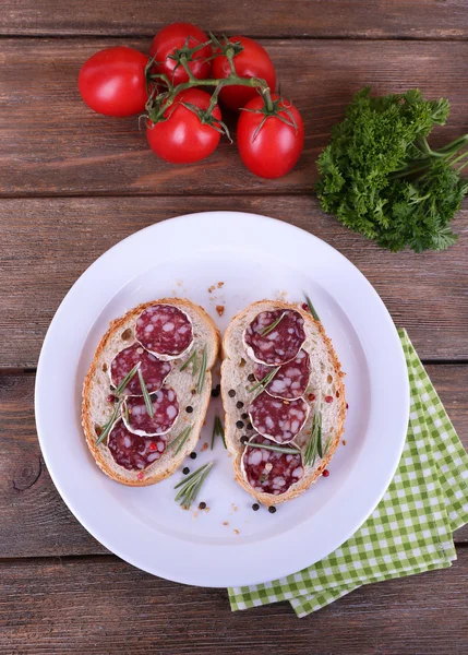 Broodjes met salami op plaat op servet op houten achtergrond — Stockfoto