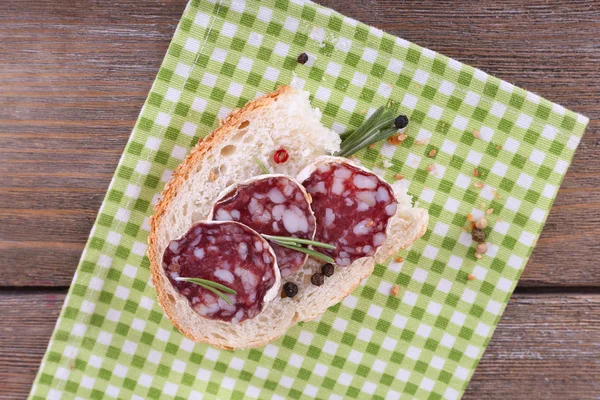 Sandwich with salami on napkin on wooden background — Stock Photo, Image