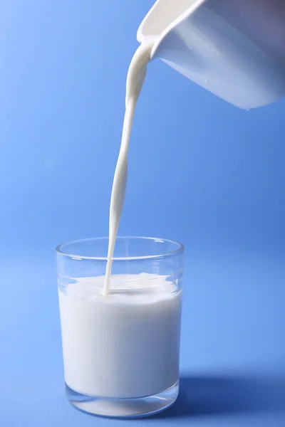 Pours milk in glass on blue background — Stock Photo, Image