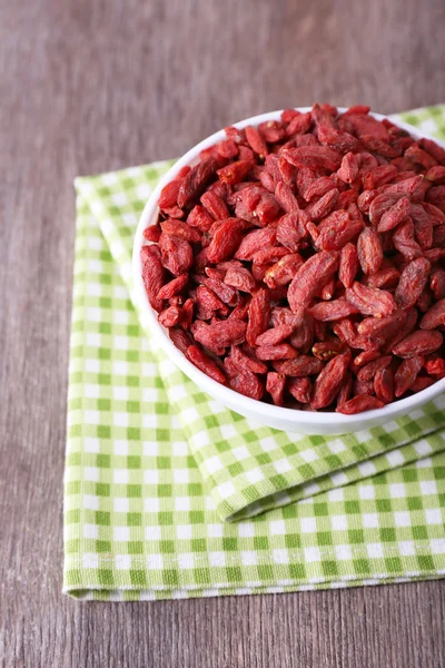 Bayas de Goji en tazón blanco sobre servilleta a cuadros sobre fondo de madera — Foto de Stock