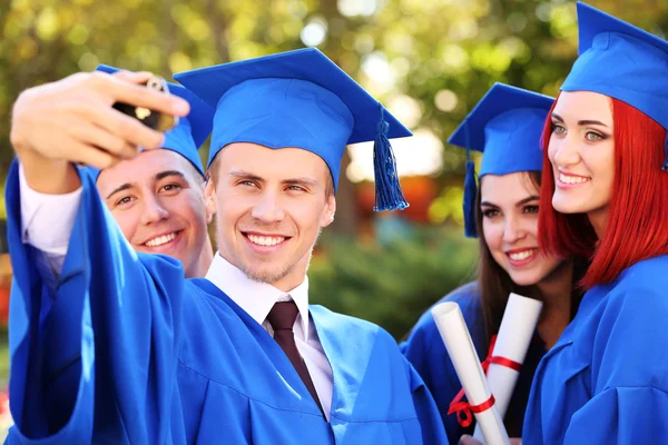 Postgraduální studenti nosí promoce čepici a šaty, venku — Stock fotografie