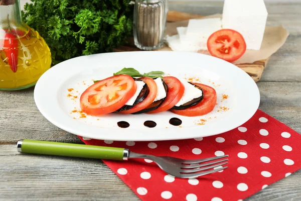 Auberginensalat mit Tomaten und Feta auf Teller, auf Serviette, auf Holzgrund — Stockfoto