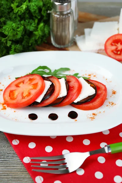 Ensalada de berenjena con tomates y queso feta en plato, en servilleta, sobre fondo de madera — Foto de Stock