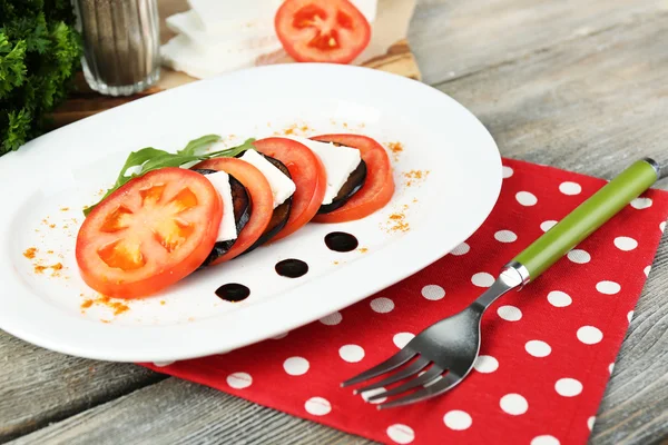 Salada de berinjela com tomate e queijo feta no prato, no guardanapo, no fundo de madeira — Fotografia de Stock