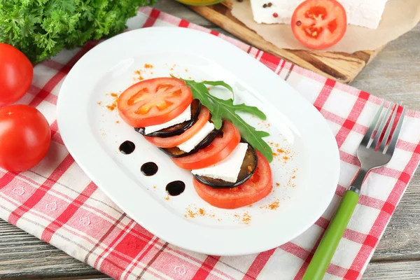 Auberginensalat mit Tomaten und Feta auf Teller, auf Serviette, auf Holzgrund — Stockfoto