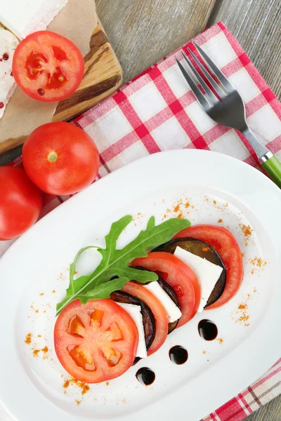 Auberginensalat mit Tomaten und Feta auf Teller, auf Serviette, auf Holzgrund — Stockfoto