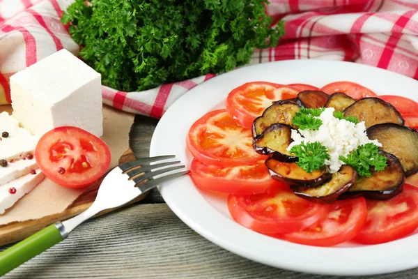 Eggplant salad with tomatoes and feta cheese, on napkin, on wooden background — Stock Photo, Image