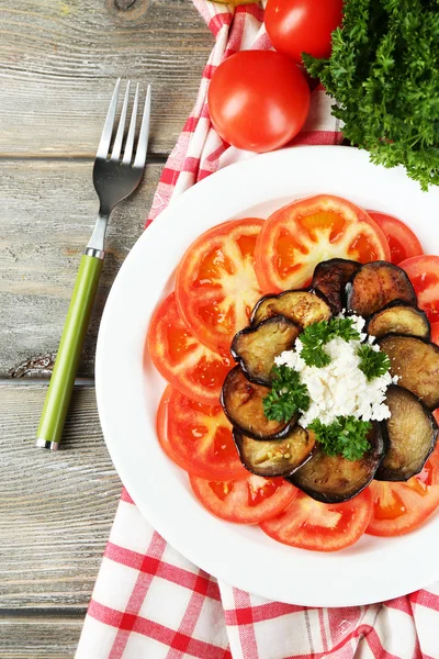 Eggplant salad with tomatoes and feta cheese, on napkin, on wooden background — Stock Photo, Image