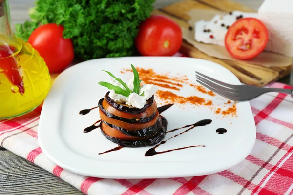 Ensalada de berenjena con tomates y queso feta en plato, en servilleta, sobre fondo de madera — Foto de Stock