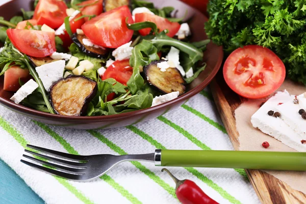 Eggplant salad with tomatoes, arugula and feta cheese, on napkin, on color wooden background — Stock Photo, Image