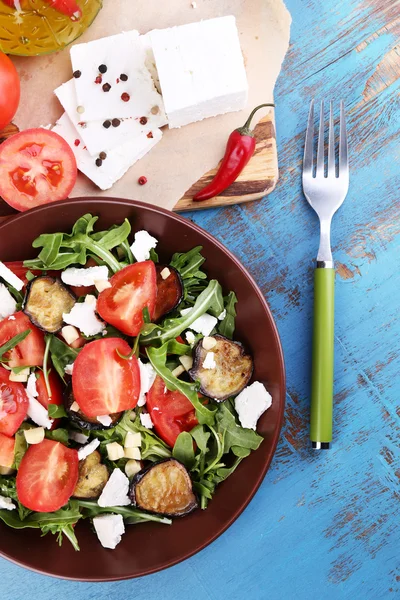 Eggplant salad with tomatoes, arugula and feta cheese, on napkin, on color wooden background — Stock Photo, Image