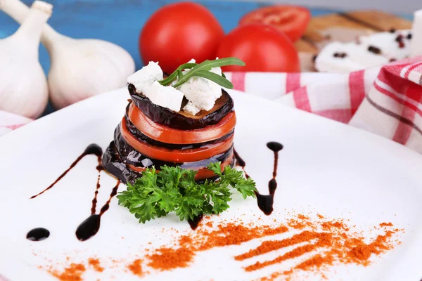 Eggplant salad with tomatoes and feta cheese on plate, on napkin,  on wooden background — Stock Photo, Image
