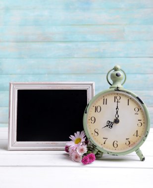 Saat ve açık mavi renkli masaya kara tahta ile güzel çiçekler