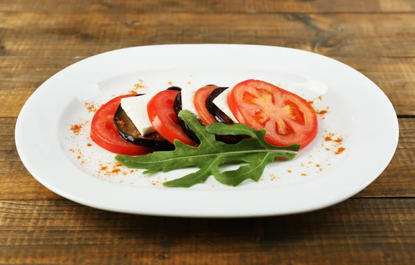 Salada de berinjela com tomate e queijo feta no prato, no fundo de madeira — Fotografia de Stock