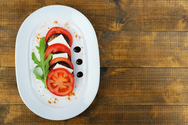 Eggplant salad with tomato and feta cheese on plate, on wooden background — Stock Photo, Image