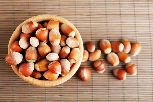 Hazelnuts in wooden bowl on bamboo mat background — Stock Photo, Image