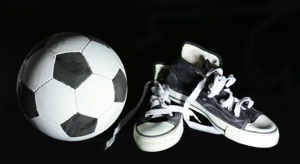 Soccer ball and sneakers on black background — Stock Photo, Image