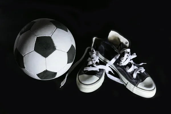 Soccer ball and sneakers on black background — Stock Photo, Image