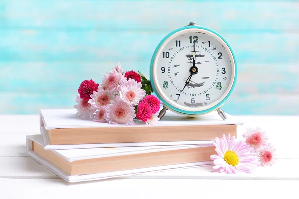 Hermosas flores con reloj y libro en la mesa sobre fondo azul claro —  Fotos de Stock