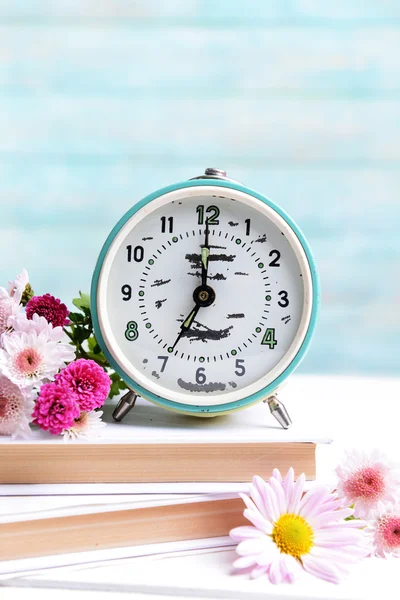 Beautiful flowers with clock and book on table on light blue background — Stock Photo, Image