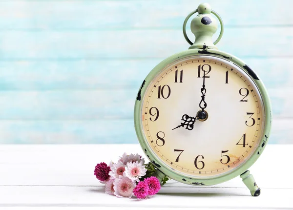 Hermosas flores con reloj en la mesa sobre fondo azul claro —  Fotos de Stock