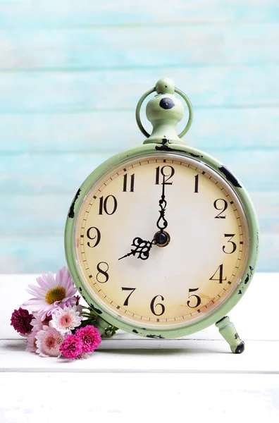 Beautiful flowers with clock on table on light blue background — Stock Photo, Image