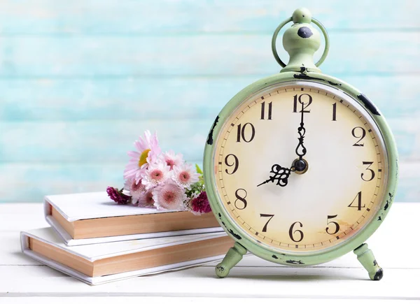 Beautiful flowers with clock and book on table on light blue background