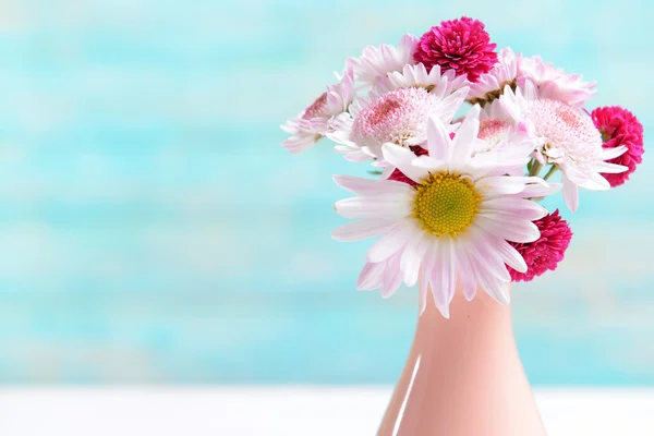 Hermosas flores en jarrón en la mesa sobre fondo azul claro —  Fotos de Stock