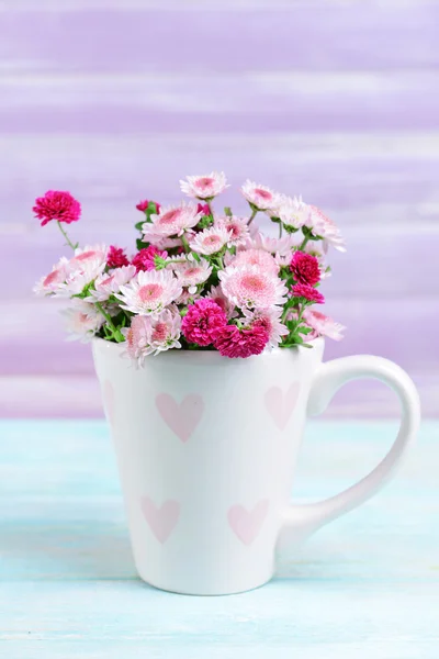 Mooie bloemen in cup op tabel op paarse achtergrond — Stockfoto