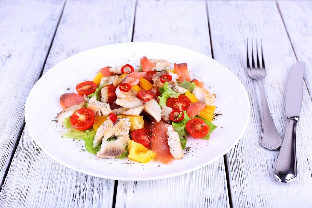 Fresh fish salad with vegetables on plate on wooden table close-up