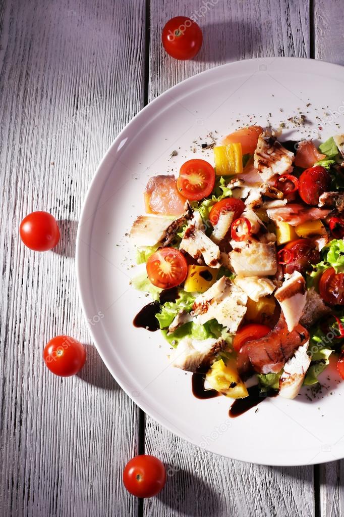 Fresh fish salad with vegetables on plate on wooden table close-up