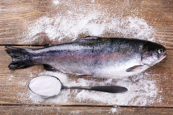 Peixe fresco e sal em colher no fundo de madeira — Fotografia de Stock