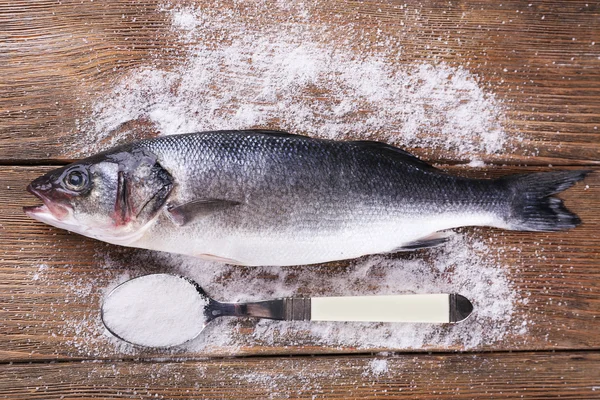 Свежая рыба и соль в ложке на деревянном фоне — стоковое фото