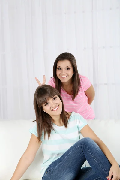 Piękne dziewczyny bliźniaki siedzi na kanapie w pokoju — Zdjęcie stockowe