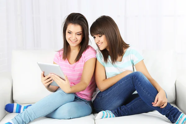 Vackra flickor tvillingar med elektroniska tablett på soffa — Stockfoto