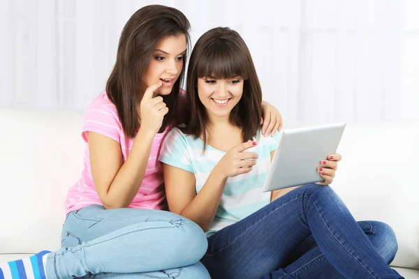 Hermosas chicas gemelas con tableta electrónica en el sofá — Foto de Stock