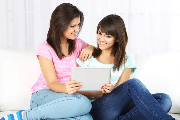 Meninas bonitas gêmeos com tablet eletrônico no sofá — Fotografia de Stock