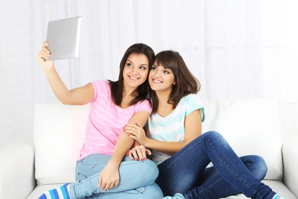 Hermosas chicas gemelas con tableta electrónica en el sofá — Foto de Stock