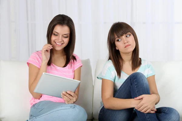 Belle ragazze gemelle con tablet elettronico sul divano — Foto Stock