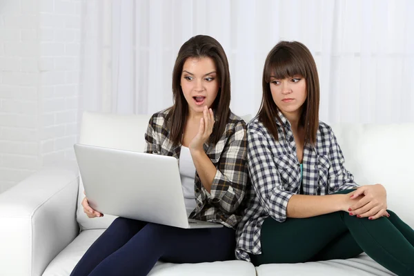 Mooie meisjes tweeling zittend op de Bank met laptop — Stockfoto