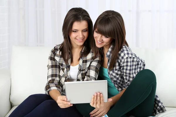 Hermosas chicas gemelas con tableta electrónica en el sofá —  Fotos de Stock