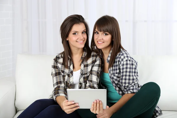 Hermosas chicas gemelas con tableta electrónica en el sofá —  Fotos de Stock