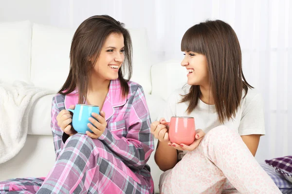 Beautiful girls twins in pajamas drinking tea at home — Stock Photo, Image
