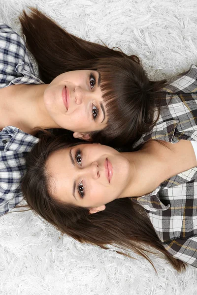 Beautiful girls twins in pajamas lie on carpet — Stock Photo, Image