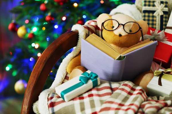 Urso de pelúcia com livro e caixas de presente em cadeira de balanço no fundo da árvore de Natal — Fotografia de Stock